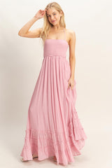 woman wearing a light pink maxi dress with a smocked bodice and ruffled hem, styled with spaghetti straps