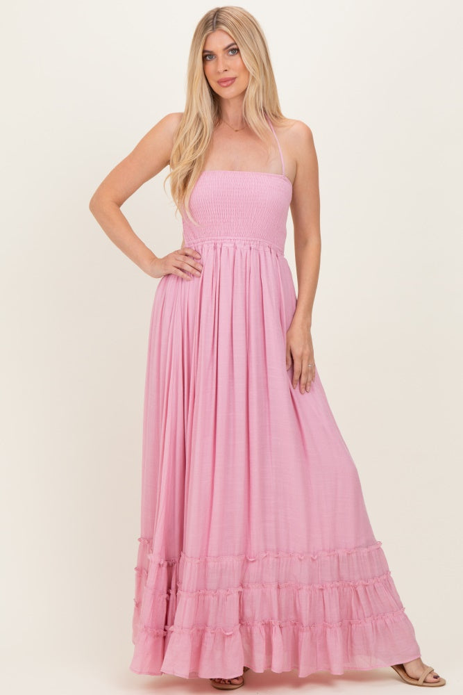 woman wearing a pink maxi dress with a smocked bodice and tiered ruffle hem, standing with one hand on her hip