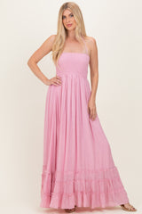 woman wearing a pink maxi dress with a smocked bodice and tiered ruffle hem, standing with one hand on her hip