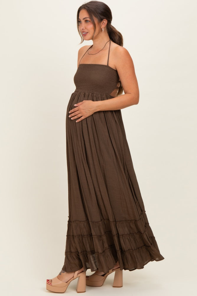 woman wearing a brown maternity maxi dress with a smocked bodice and tiered skirt, gently holding her baby bump