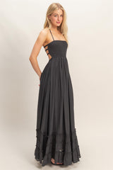 woman wearing a black maxi dress with a smocked bodice and ruffled hem, featuring back cutouts and adjustable straps