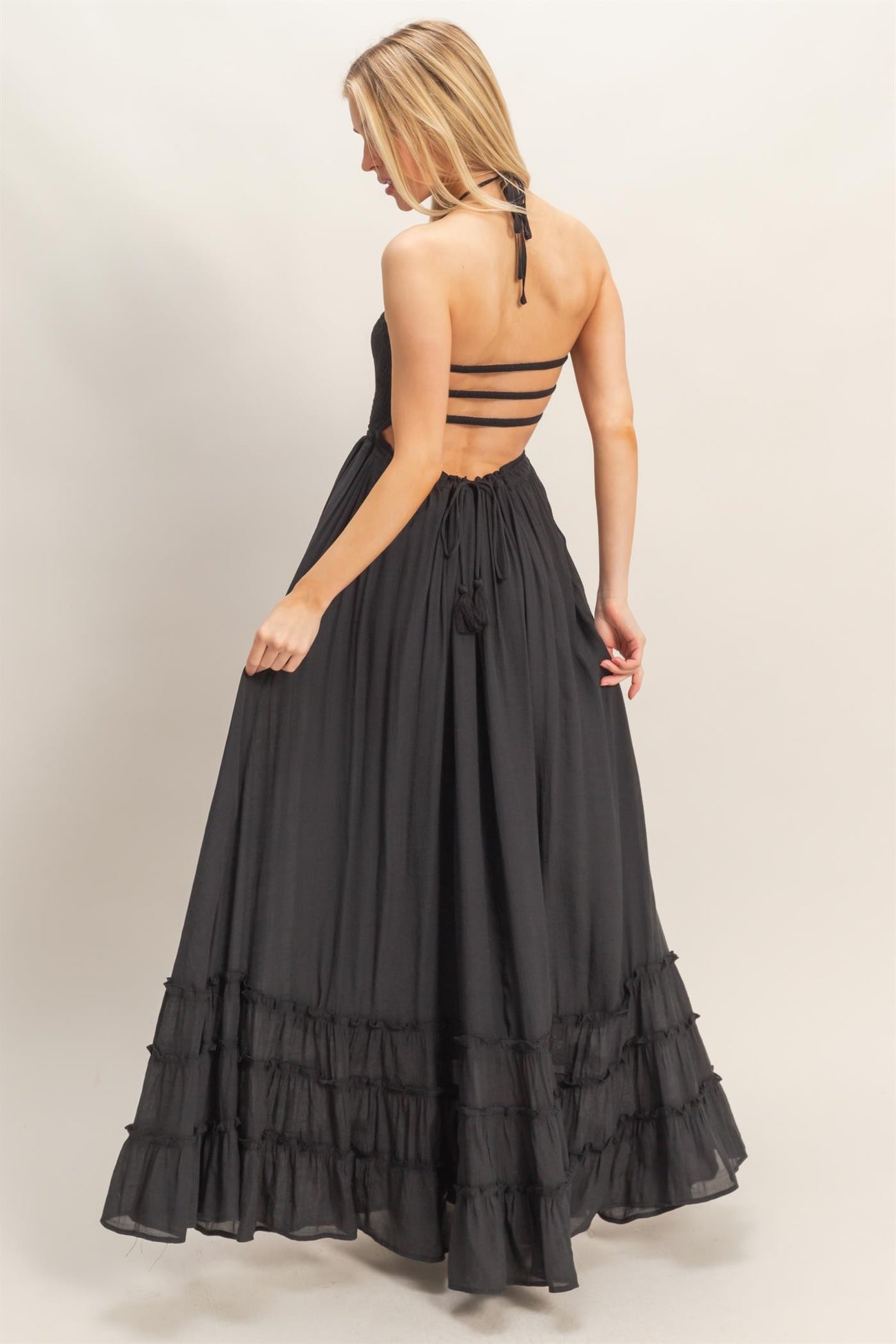 woman wearing a black maxi dress with a plunging back and ruffle hem, showcasing a strappy back design
