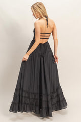 woman wearing a black maxi dress with a plunging back and ruffle hem, showcasing a strappy back design