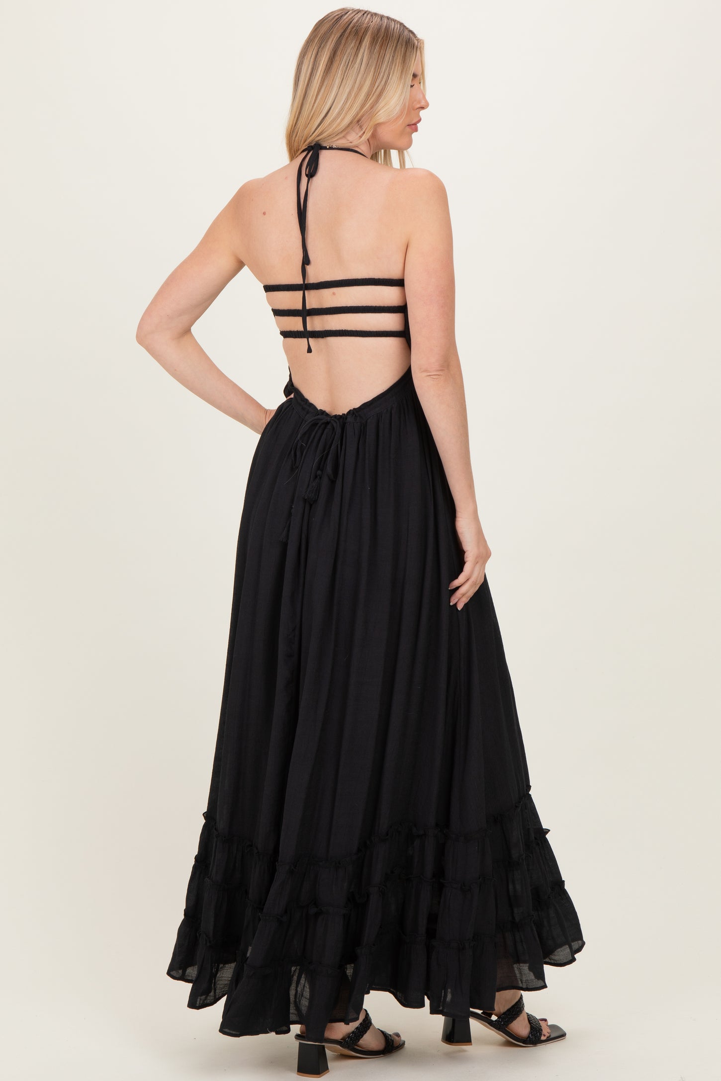 woman wearing a black halter neck maxi dress with tiered ruffles and open back details