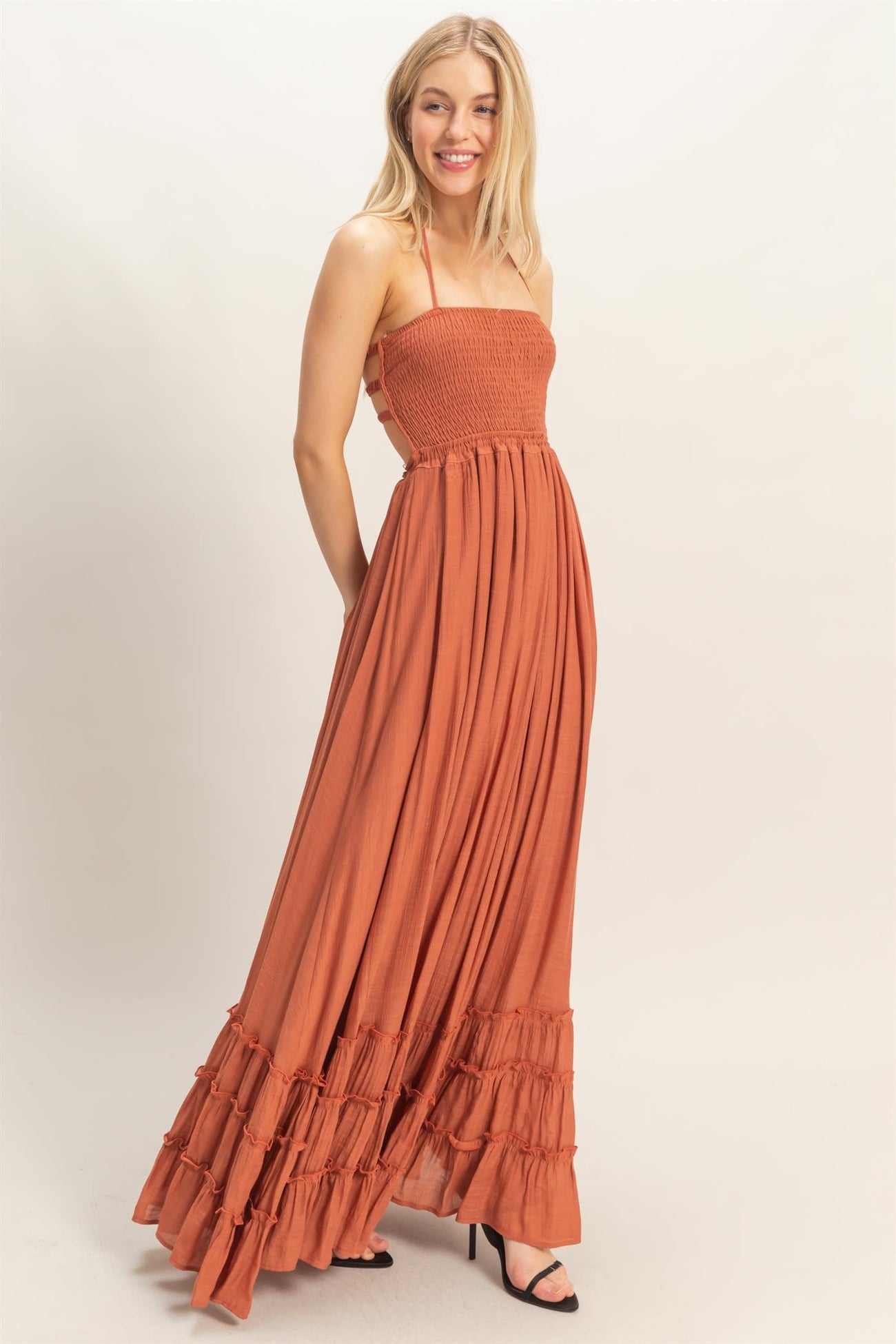 woman wearing an orange smocked maxi dress with ruffle details and spaghetti straps, standing and smiling