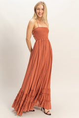woman wearing an orange smocked maxi dress with ruffle details and spaghetti straps, standing and smiling