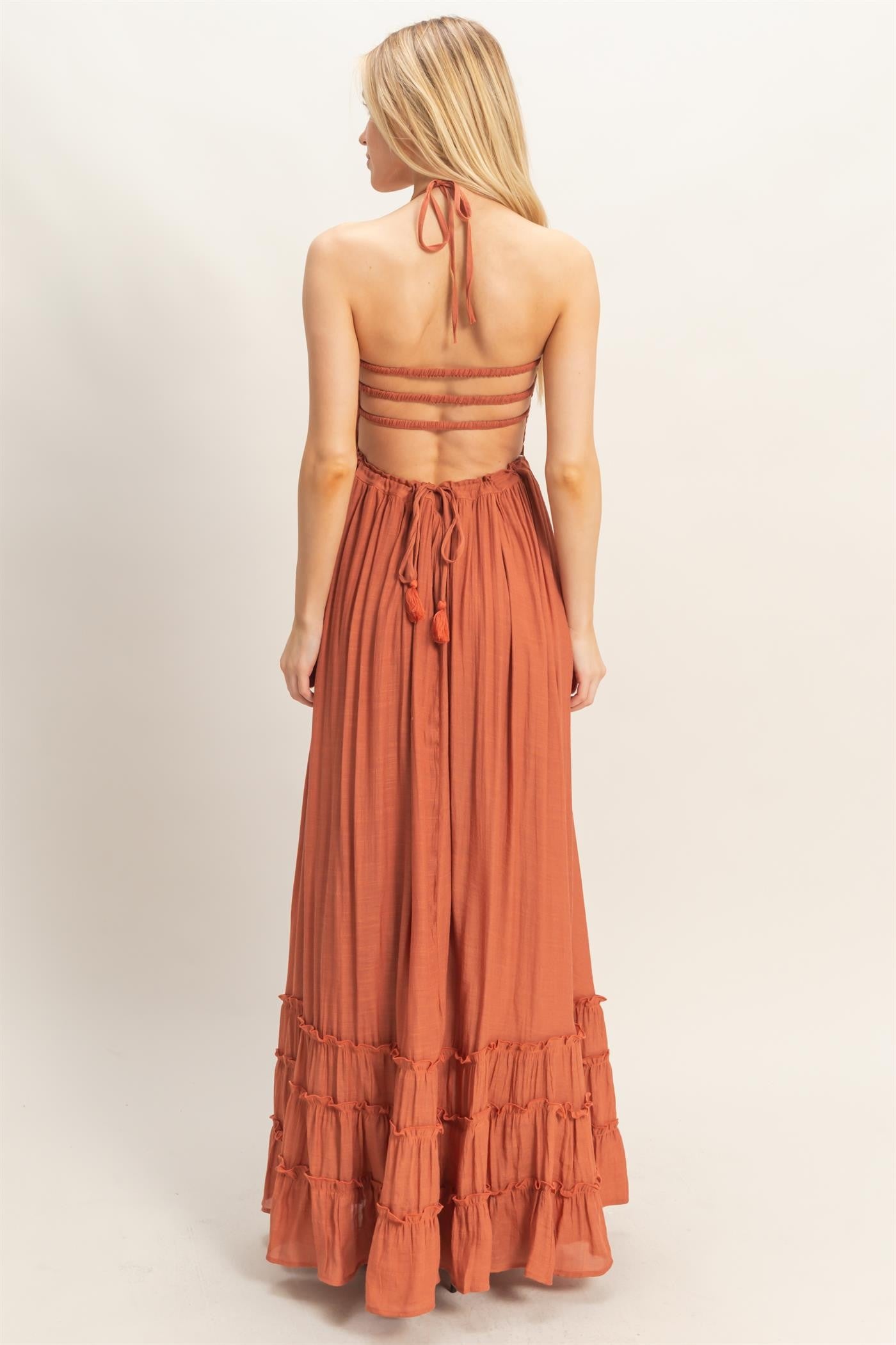 woman wearing a rust-colored maxi dress with a halter neck and tiered ruffle hem, showing a tied back design