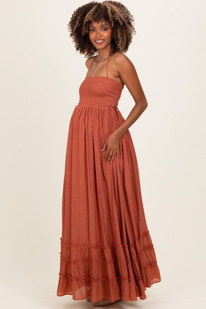 woman wearing a rust colored maxi maternity dress with a smocked bodice and ruffled hem, highlighting her baby bump
