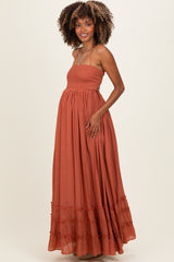 woman wearing a rust colored maxi maternity dress with a smocked bodice and ruffled hem, highlighting her baby bump