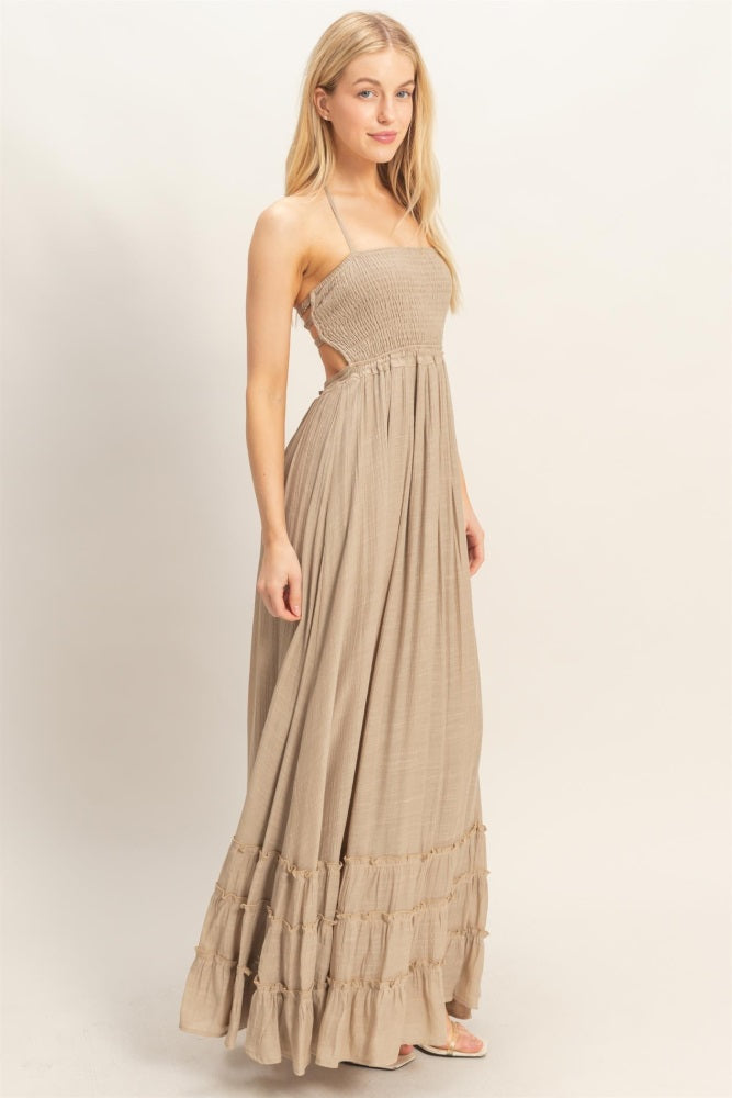 woman wearing a beige maxi dress with a smocked bodice and tiered ruffle detailing at the hem