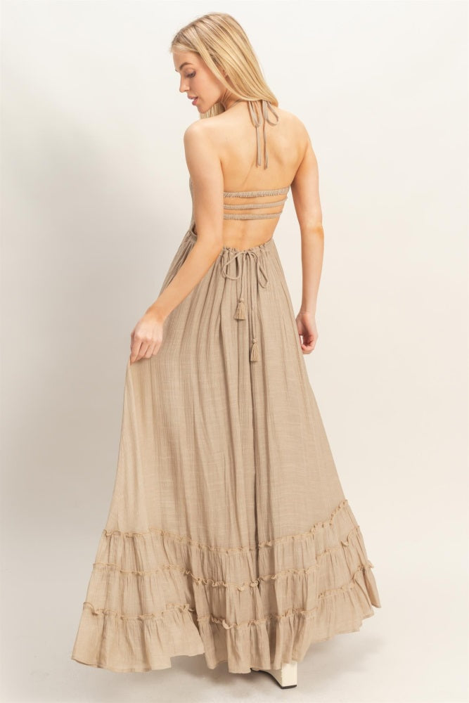 woman wearing a beige halter neck maxi dress with a ruffled hem and open back detail