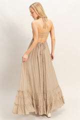 woman wearing a beige halter neck maxi dress with a ruffled hem and open back detail