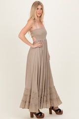 woman wearing a taupe maxi dress with smocked bodice and tiered ruffle hem, standing sideways with a relaxed pose