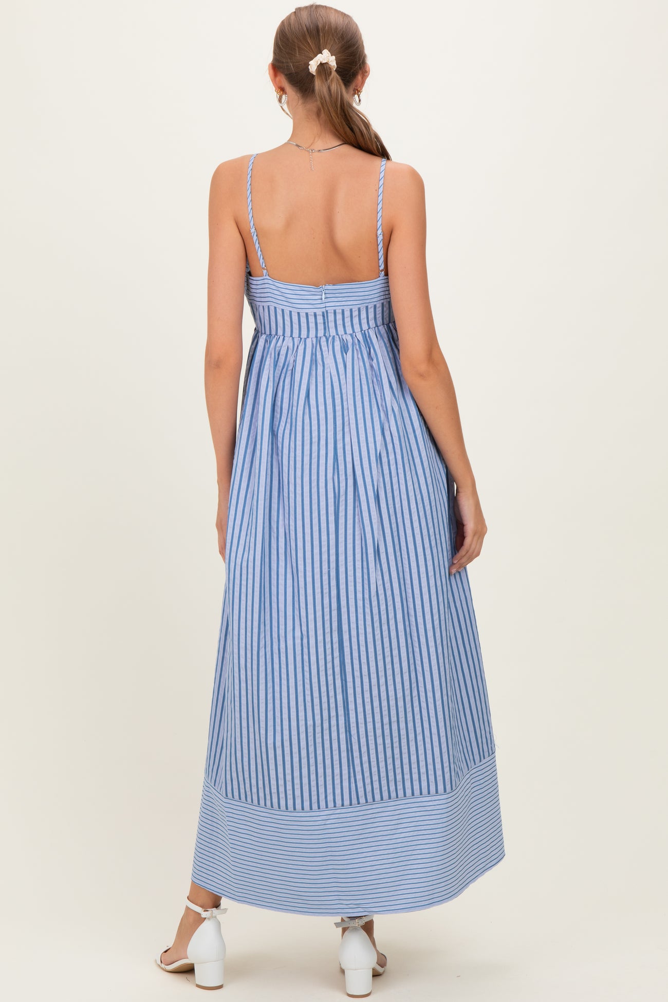 woman wearing a blue and white striped maternity maxi dress with spaghetti straps, showcasing her back and flowing design