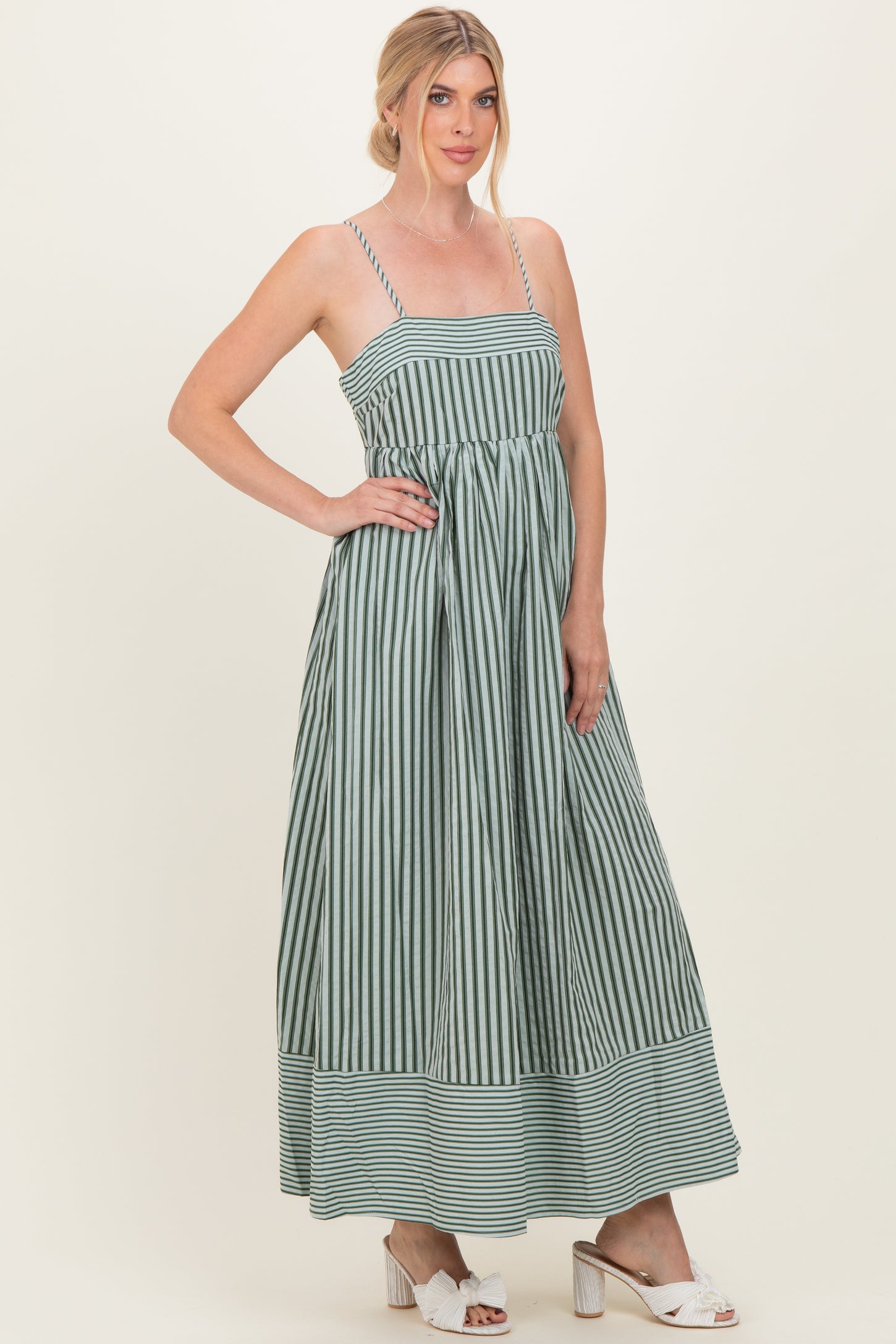 woman wearing a green and white striped maxi dress with thin straps and a fitted bodice