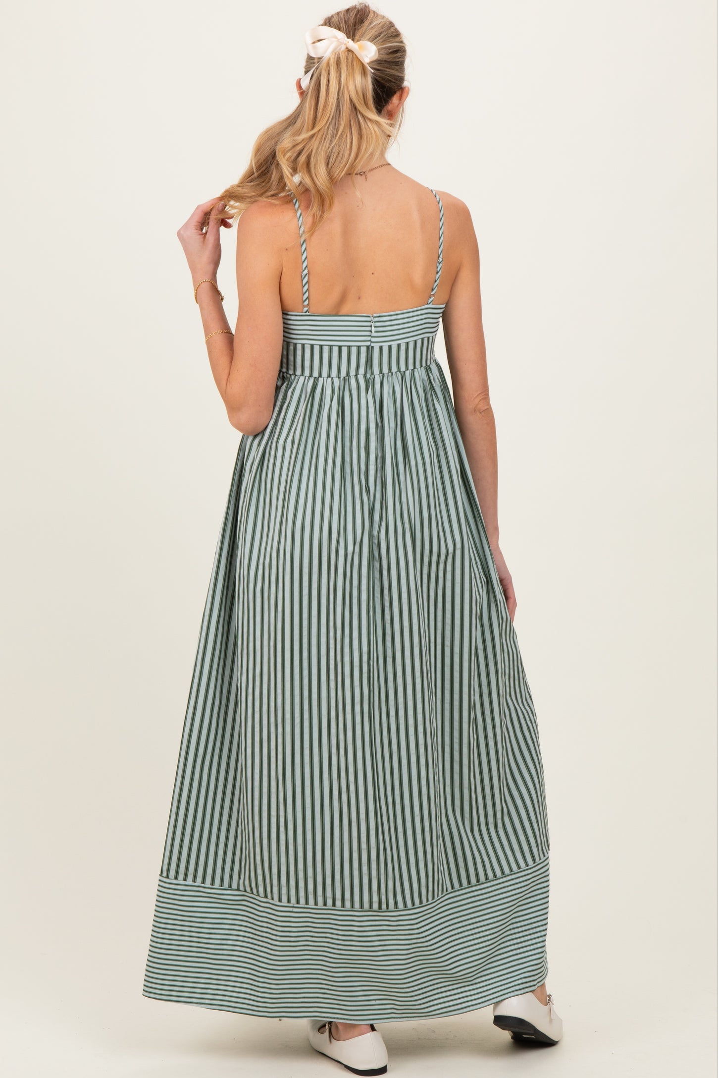 woman wearing a green and white striped maternity maxi dress with adjustable straps and a flowy silhouette