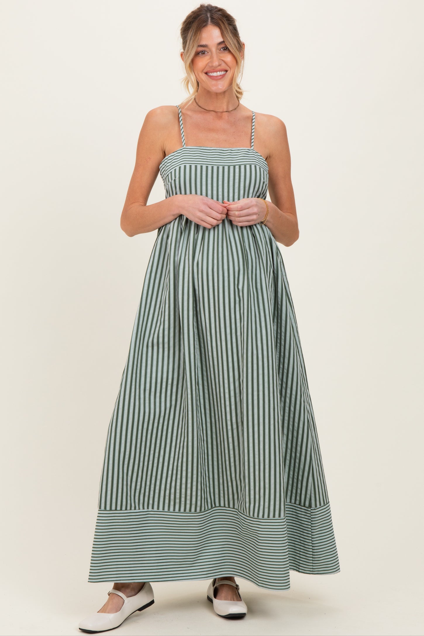 woman wearing a green and white striped maternity maxi dress with a fitted bodice and flowy skirt, baby bump visible