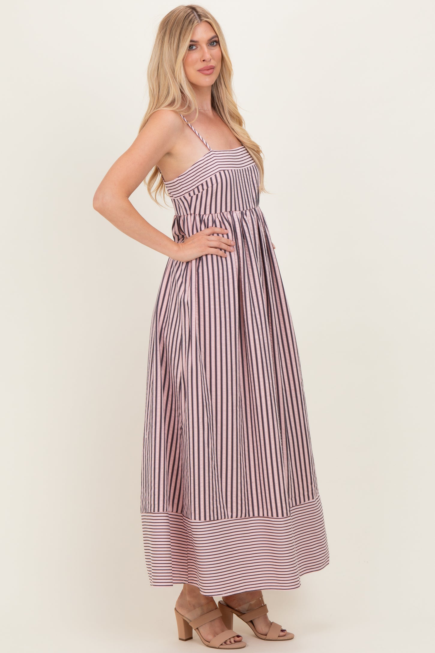woman wearing a long striped maxi dress with a fitted bodice and flared skirt, standing in profile