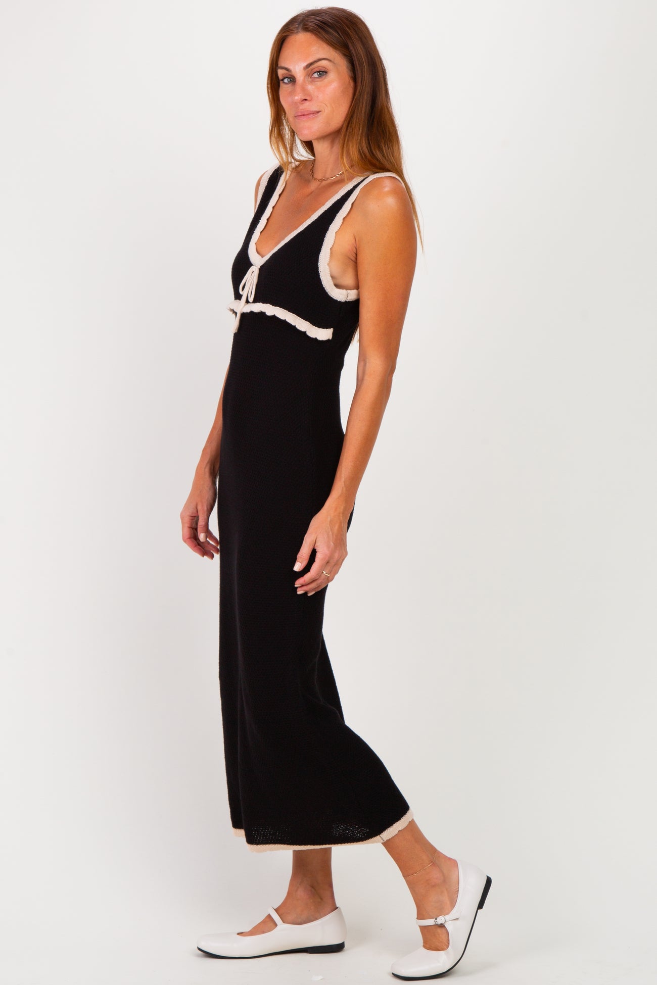 woman wearing a black maxi dress with white trim and a tie front detail, styled with white flat shoes