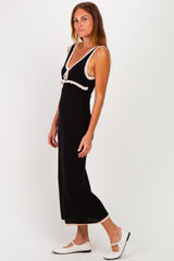 woman wearing a black maxi dress with white trim and a tie front detail, styled with white flat shoes