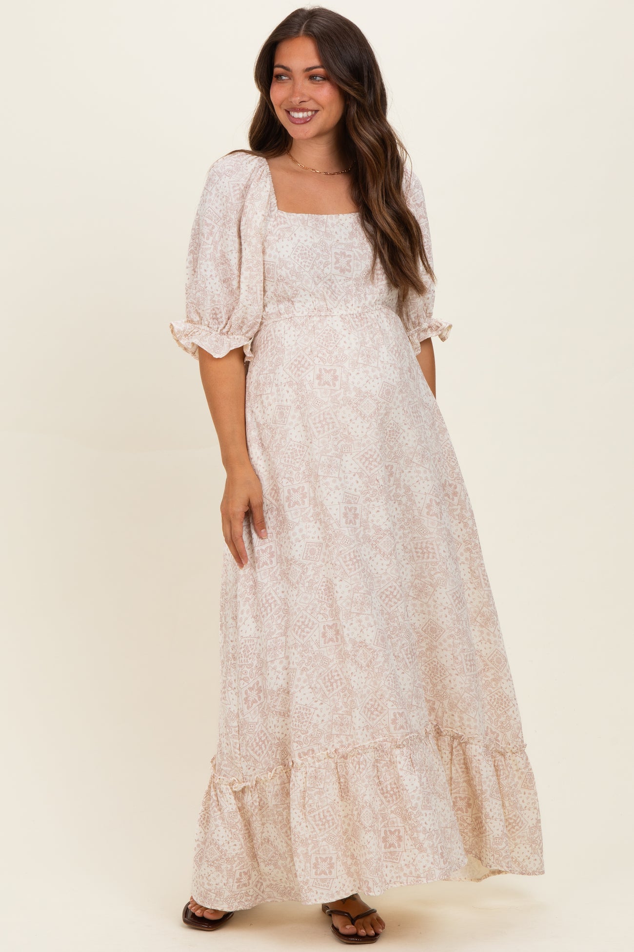 woman wearing a light pink floral maternity maxi dress with puff sleeves and a flowing skirt, baby bump visible