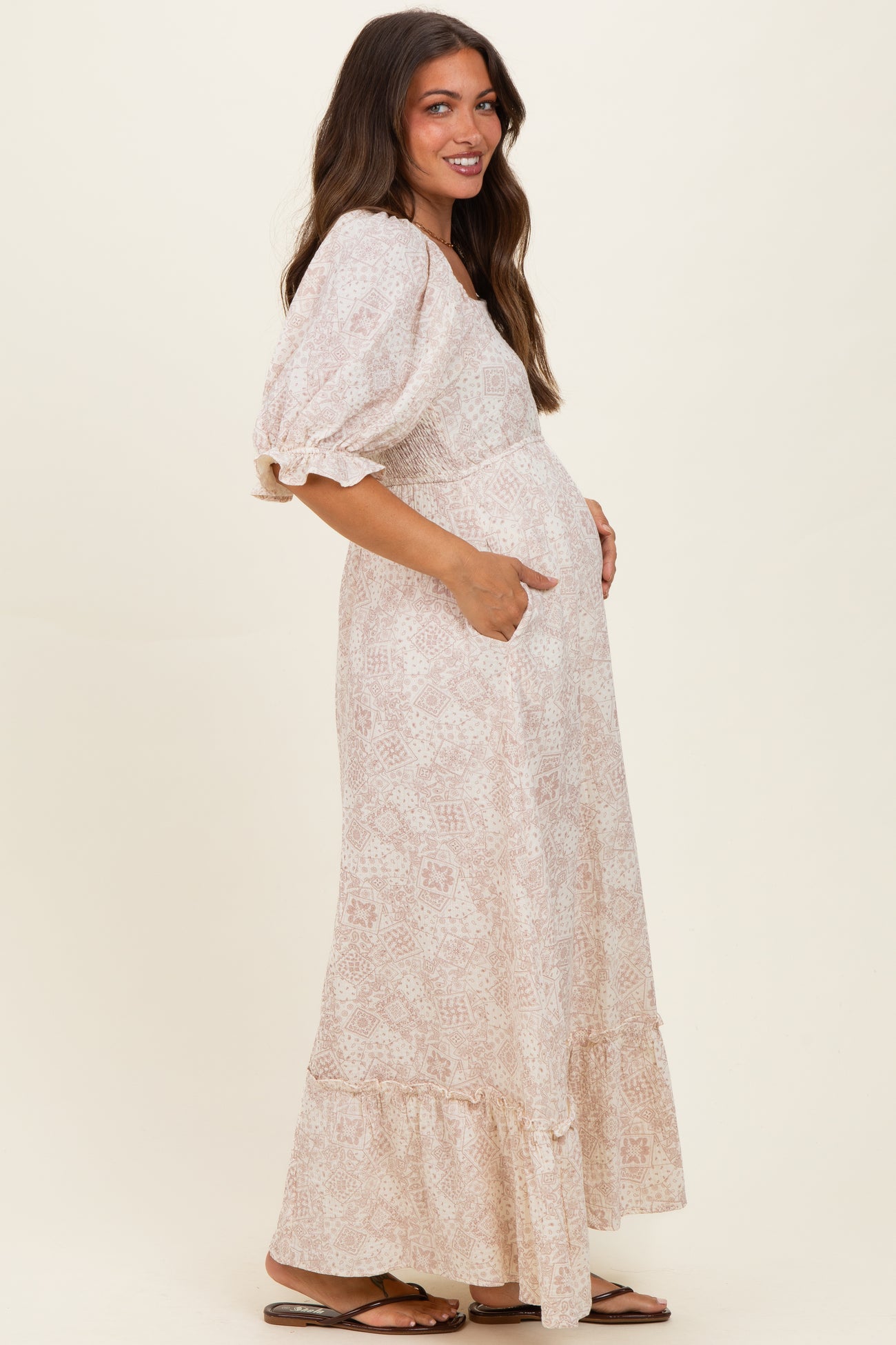 woman wearing a light pink patterned maternity maxi dress with puff sleeves and pockets, showing a baby bump