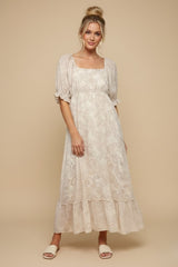 woman wearing a beige floral maxi dress with puff sleeves and a tiered skirt, standing on a neutral background