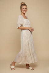 woman wearing a cream floral maxi dress with puff sleeves and a tiered skirt, standing on a beige background