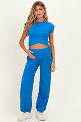 woman wearing a blue maternity crop top and matching wide-leg pants, holding her baby bump