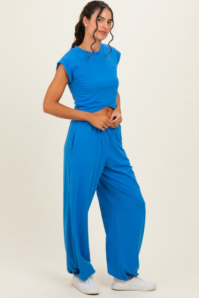 woman wearing a bright blue cropped top and matching loose-fit trousers, standing against a neutral background