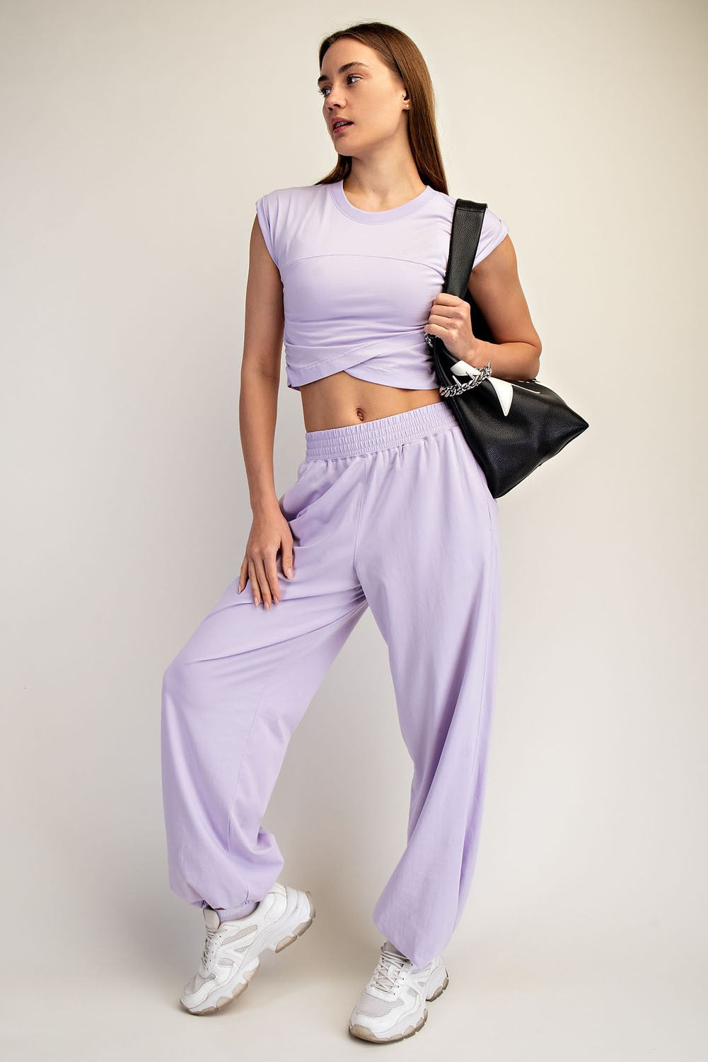 woman wearing a lavender cropped t-shirt and matching loose sweatpants, carrying a black bag, styled casually