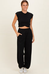 woman wearing a black sleeveless crop top and black wide-leg pants with pockets, styled with white sneakers