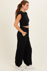 woman wearing a black cropped t-shirt and matching black wide-leg pants with pockets, styled with white sneakers