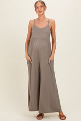 woman wearing a taupe maternity jumpsuit with pockets and adjustable straps, showcasing her baby bump