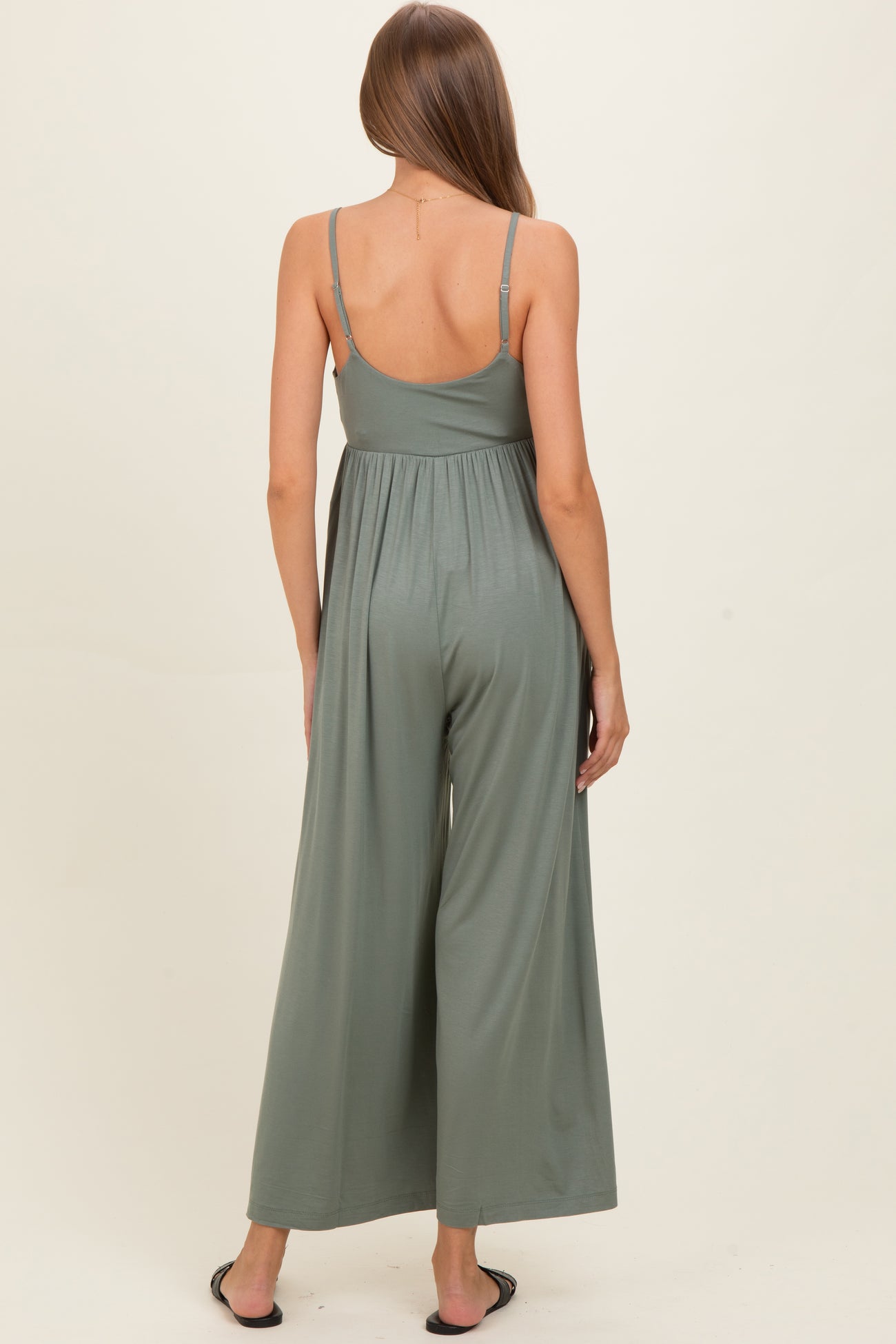 woman wearing a green maternity jumpsuit with spaghetti straps, showing a relaxed fit and draped back style