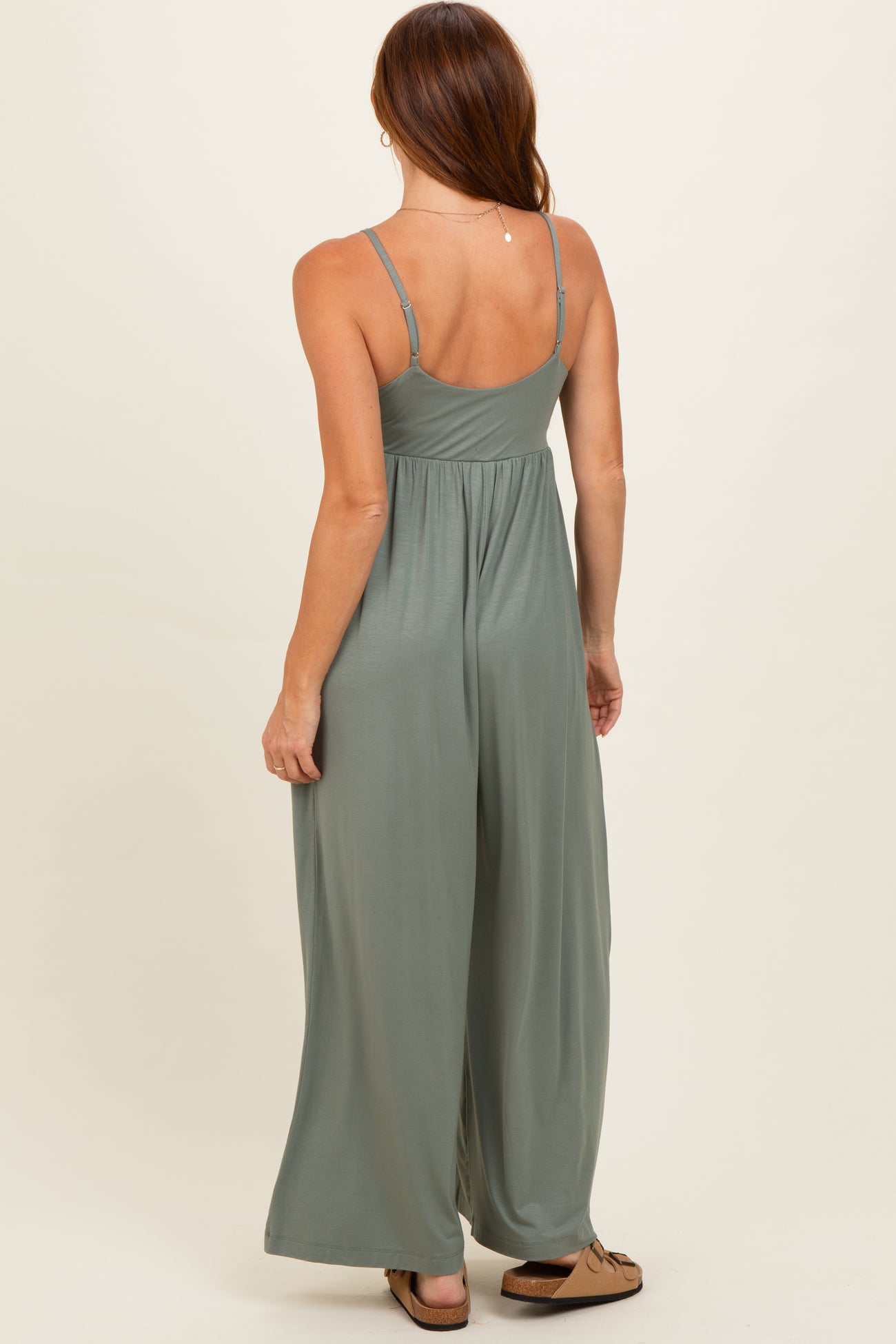 woman wearing a back view of a sage green sleeveless wide-leg jumpsuit with adjustable straps