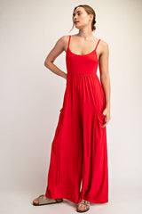 woman wearing a red sleeveless jumpsuit with wide leg and side pockets, standing with one hand on her hip