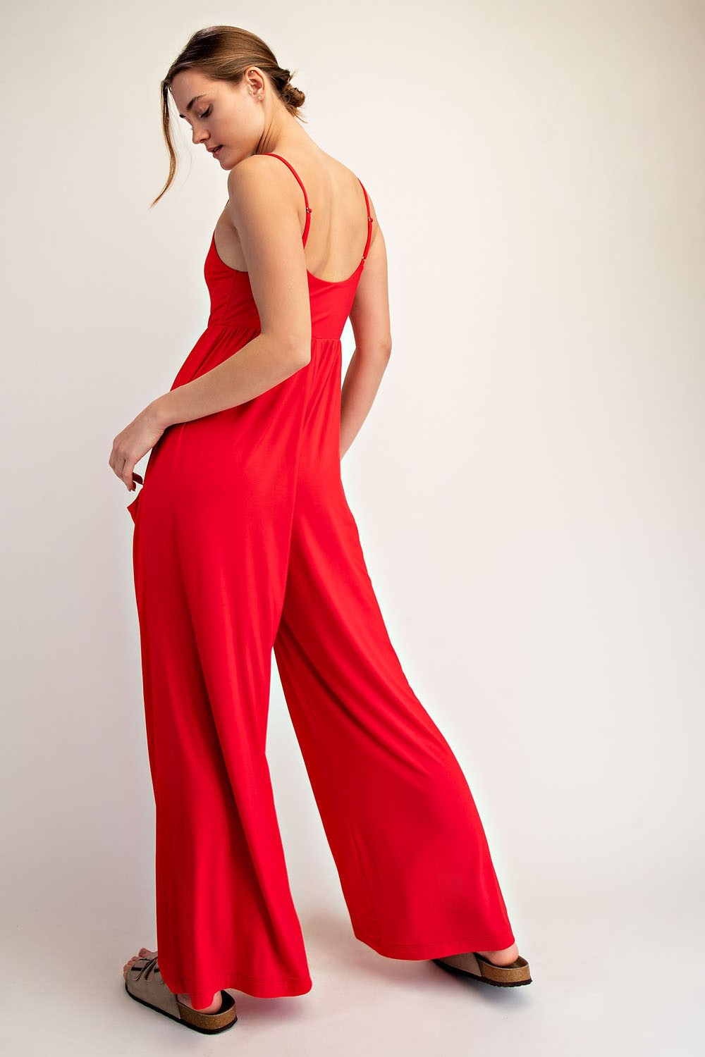 woman wearing a red sleeveless jumpsuit with wide legs, shown from the back, styled with flat sandals