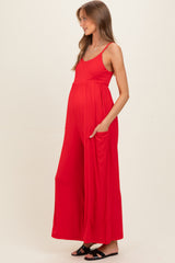 woman wearing a red maternity jumpsuit with pockets, showing her baby bump