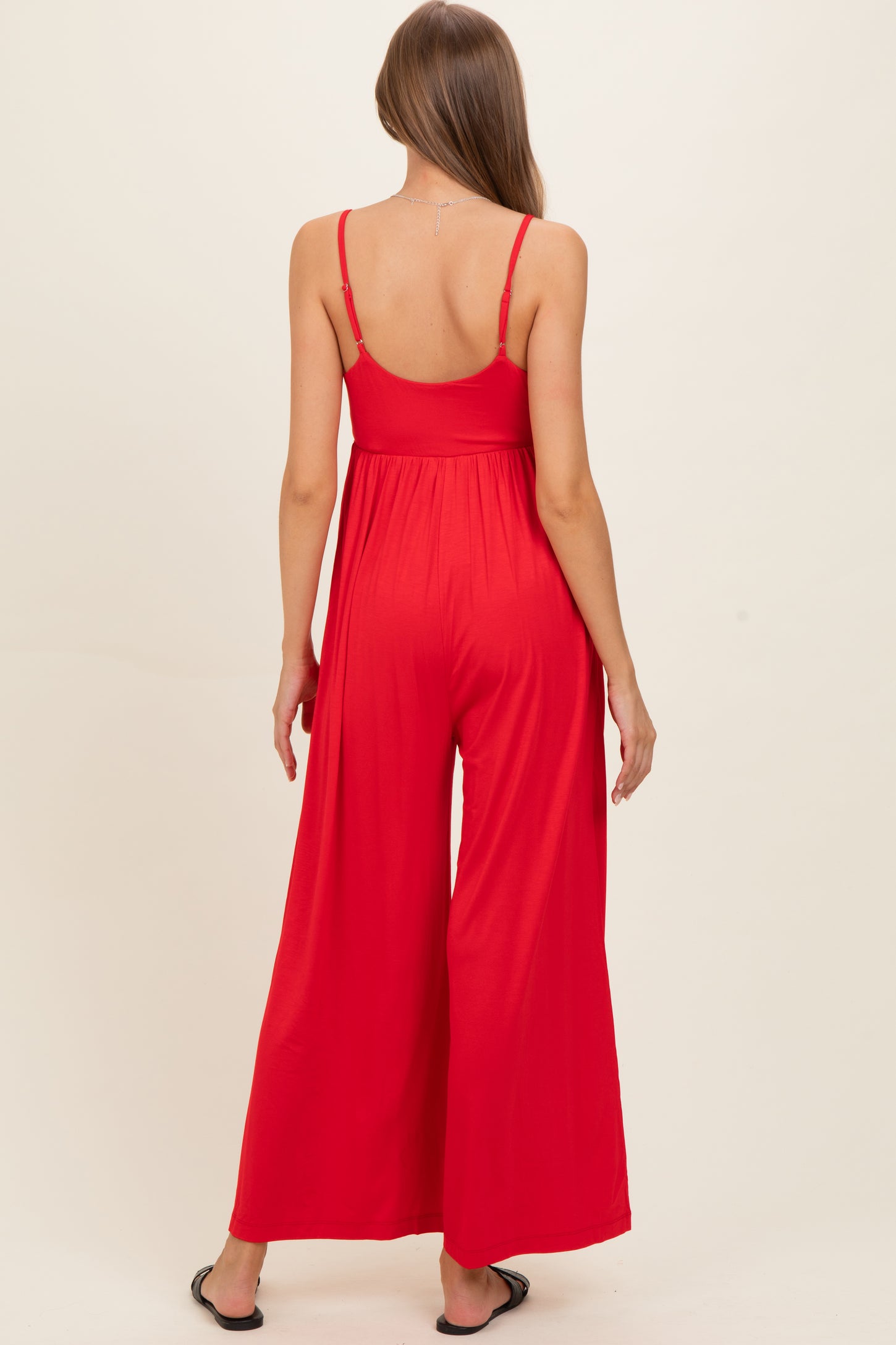 woman wearing a red maternity jumpsuit with wide legs and adjustable straps, showing a baby bump from the back