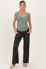 woman wearing a light green ribbed maternity top and dark gray maternity pants with pockets, displaying a baby bump