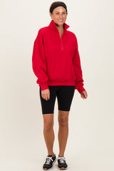 woman wearing a red quarter-zip pullover sweatshirt with black bike shorts and sneakers