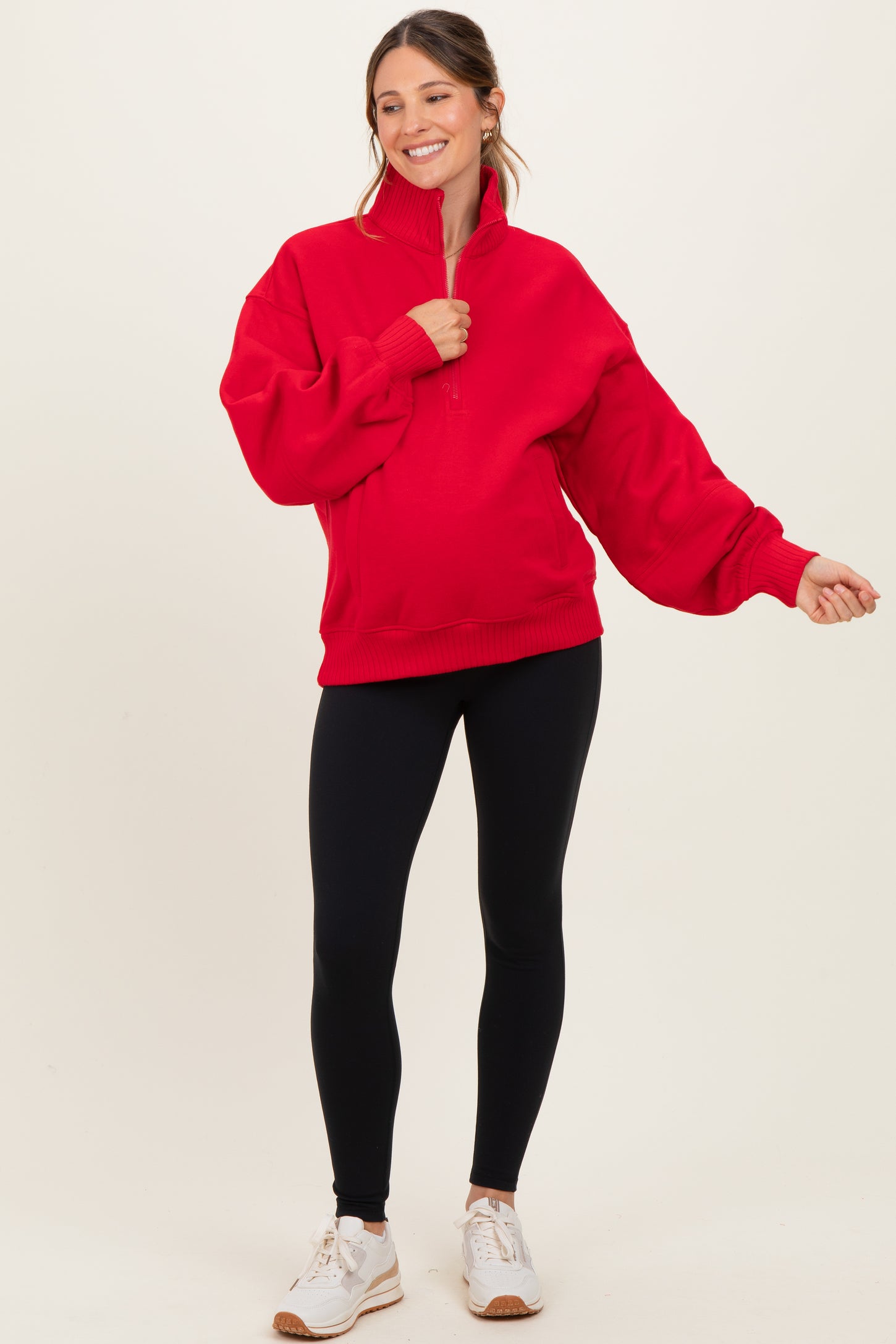 woman wearing a red maternity pullover sweatshirt with a half-zip and balloon sleeves, paired with black leggings and sneakers