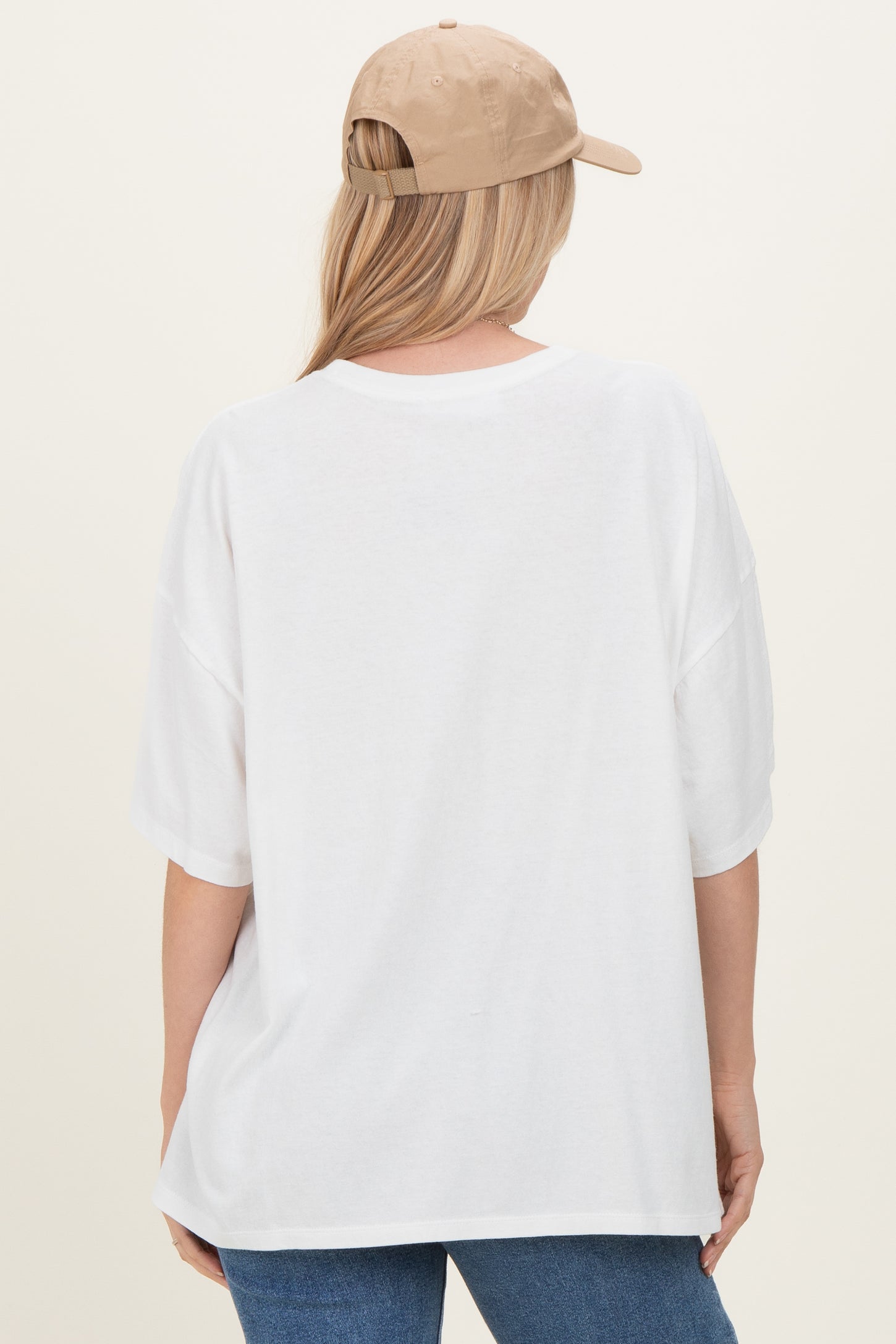woman wearing a white oversized t-shirt and a beige baseball cap, viewed from the back