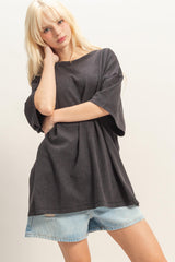 woman wearing an oversized black t-shirt and light blue denim shorts, posing with one arm crossed over her body