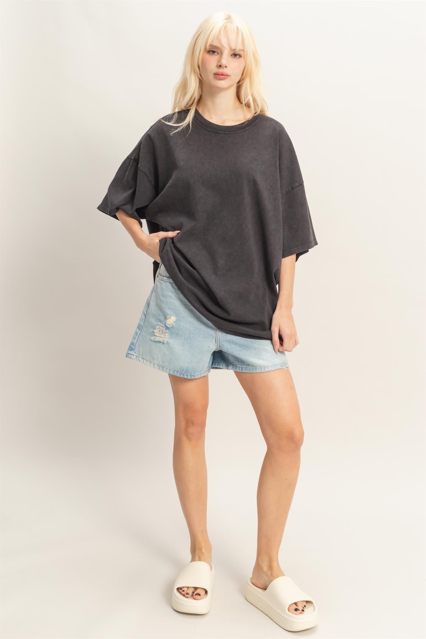 woman wearing an oversized gray t-shirt with distressed denim shorts and cream slide sandals