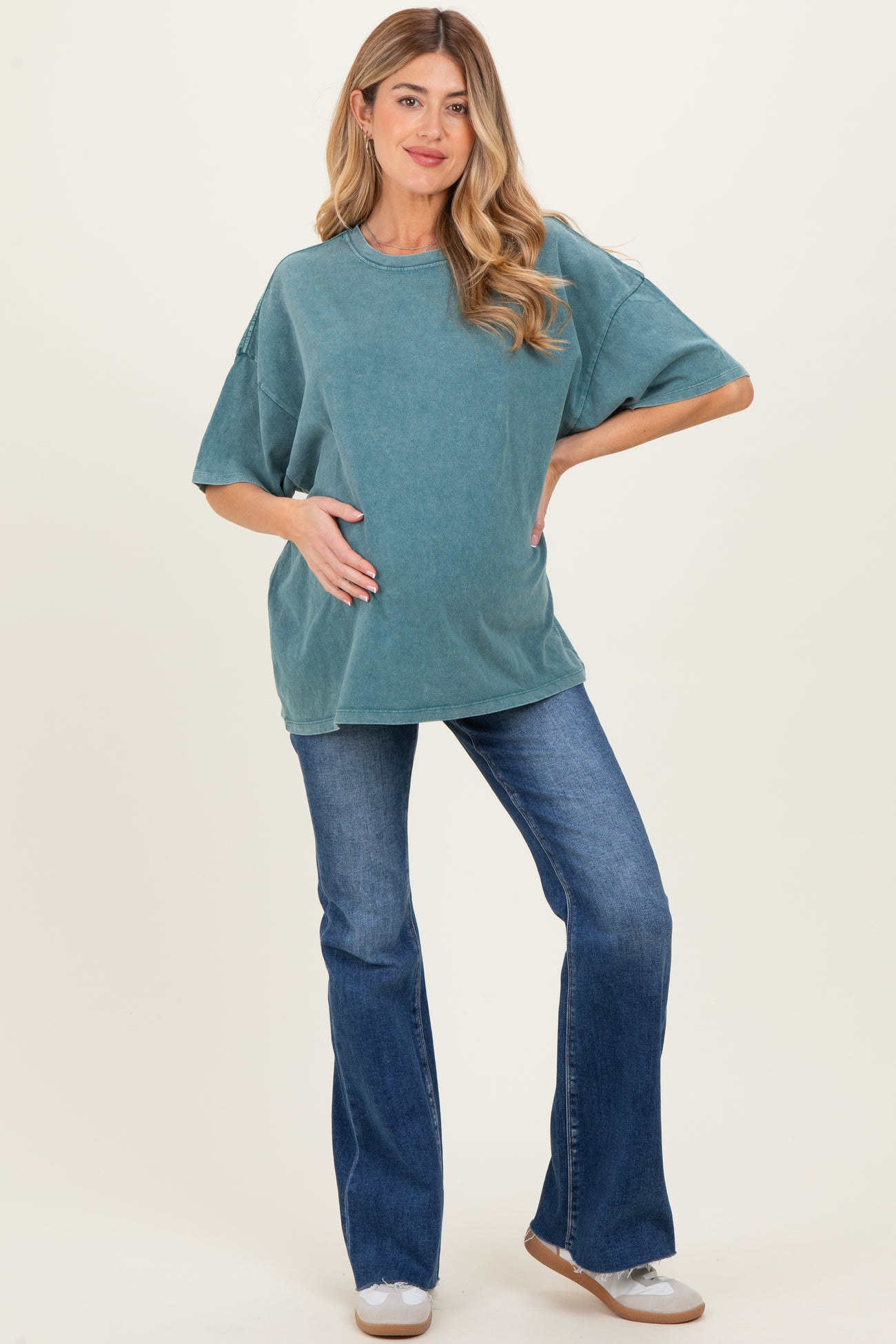 woman wearing a teal oversized maternity t-shirt and blue flared jeans, holding her baby bump