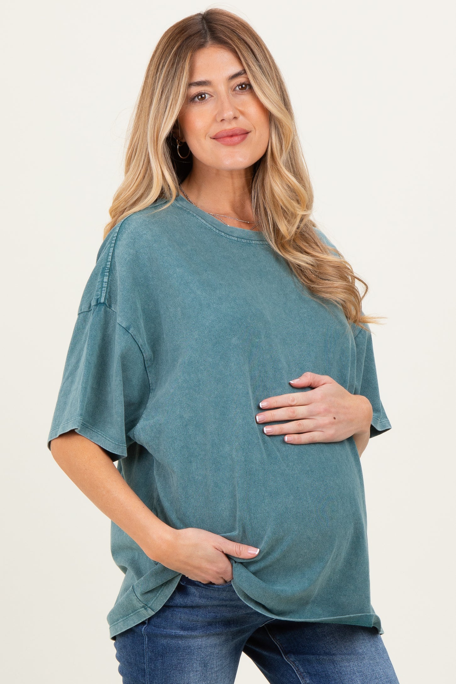 woman wearing a teal oversized maternity t-shirt and highlighting her baby bump with one hand