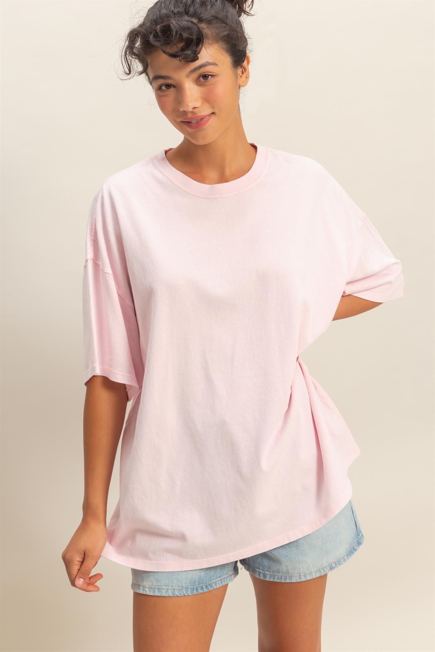 woman wearing a light pink oversized t-shirt with short sleeves and casual denim shorts