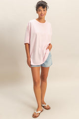 woman wearing a light pink oversized t-shirt and denim shorts, standing and smiling with casual sandals